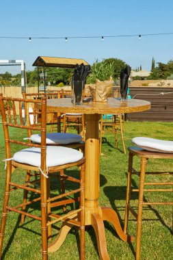 Uzun sandalyeli ahşap bir bar masası, bahçeye kurulmuş, güneşli bir günde tel ışıkların altında bir olaya hazır..