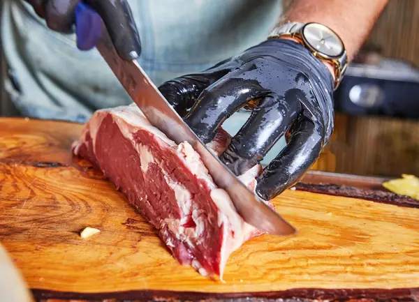 stock image A close-up of a chef using a knife to slice raw steak on a wooden cutting board, preparing meat for cooking.