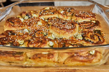 Susam tohumlarıyla kaplı cam bir kapta taze pişmiş sebze ruloları, altın rengi ve ahşap bir yüzey üzerinde servis etmeye hazır..