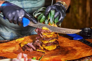 Şişe üzerine ananas istiflenmiş ızgara eti ustalıkla oyan bir şef ağız sulandırıcı bir yemek deneyimi yaratıyor..