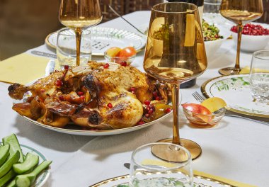Nar tohumlarıyla süslenmiş, altın kavrulmuş tavuk, yemek masasında zarif bir şekilde sunulur, bardaklar ve garnitürlerle..