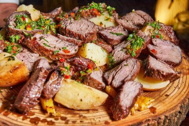 Lezzetli ızgara et dilimleri ve patatesle dolu ahşap bir tabak. Üstüne de fazladan tat vermesi için taze otlar..