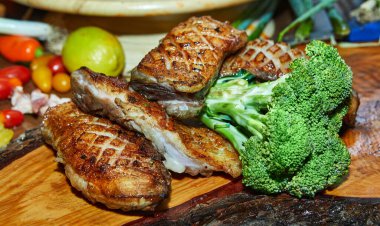 Tahta bir tahtada taze brokoliyle süslenmiş ve canlı sebzelerle çevrili sulu ızgara et..