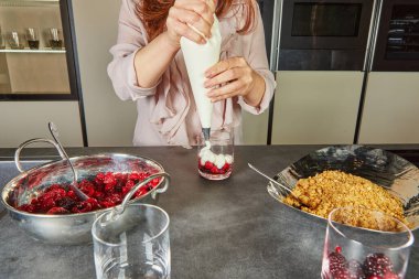 Bir insan, tatlı bardağına krema dökerek bir kat böğürtlenin üzerine krema döker ve tatlıya kremalı bir doku ekler..