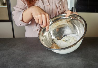 Bir insan metal bir kâsede kaşıkla karışımı karıştırır. Mutfak ortamında ev yapımı tarifin bileşenlerini birleştirir..