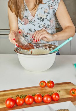 Bir kadın hamurla dolu bir karıştırma kabına domates yapıştırıcısı döker ve mutfakta lezzetli bir yemek hazırlar..