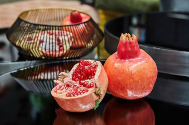 Tam ve yarım nar, arka planda bitkiler bulunan şık bir mutfak ve dinlenme odasındaki dekoratif bir masada oturur..