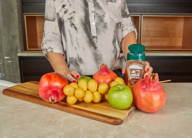 Nar, elma, üzüm ve bal içeren taze meyve seçimi ahşap bir kesim tahtasının üzerinde sergilenmektedir..