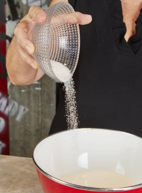 Sugar being poured from a clear bowl into a mixing bowl, preparing ingredients for a dessert in the kitchen. clipart