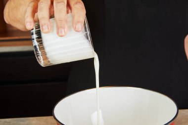 Beyaz bir karıştırma kabına süt döken bir el modern bir mutfak ortamında yemek tarifi hazırlıyor..