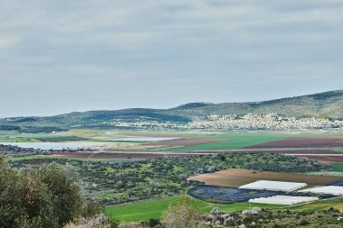 Geniş bir kırsal alan, ekili tarlalar, yeşillik alanları ve kayan tepelere karşı kurulmuş uzak bir köy..