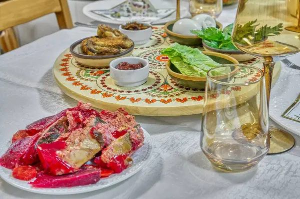 Hamursuz Bayramı sofrası, matza, sembolik yeşiller ve zarif cam örtülerle çevrili süslü bir seder tabağı..