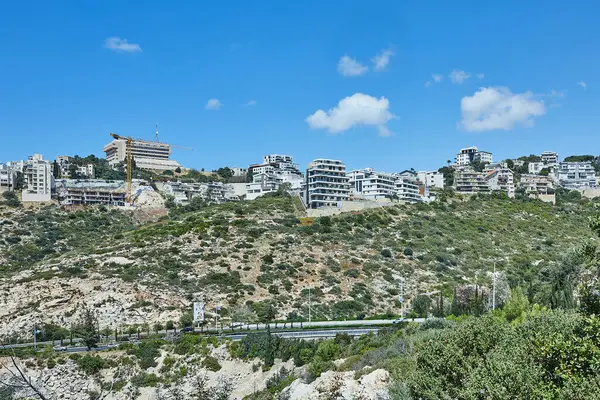 Yeşil yamaçlara tepeden bakan konut evleri ve parlak mavi bir gökyüzü, huzur dolu banliyö dağlarını yakalıyor..