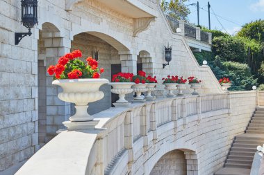 İsrail 'in Haifa kentindeki Bahai Bahçeleri' nde güneşli gökyüzünün altında canlı kırmızı çiçeklerle bezenmiş süslemeli beyaz kayalar..