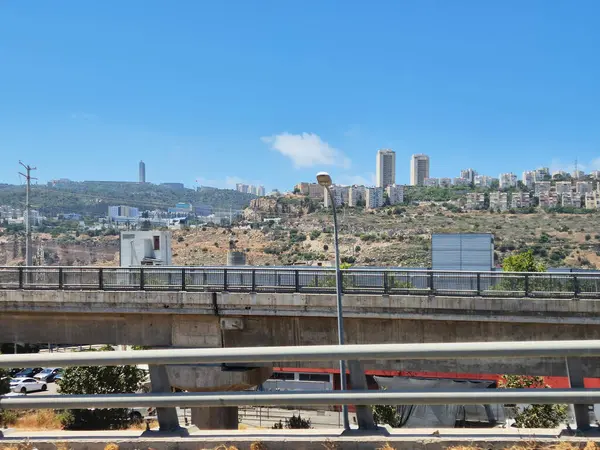 Vadiyi geçen üstgeçit köprüsüne sahip kentsel altyapı, tepelerde yüksek binalar ve yukarıda açık güneşli bir gökyüzü..