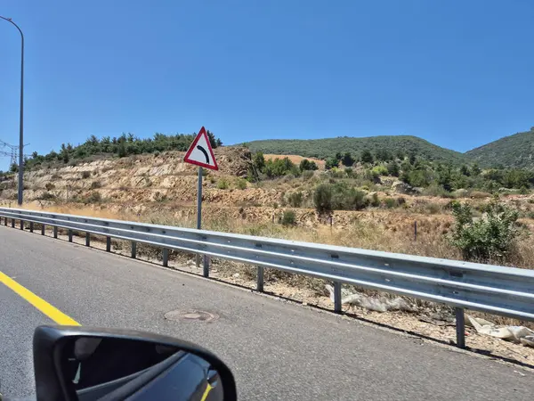 Kuru kayalık tepelerde kıvrımlı bir kırsal yol. Trafik işaretleri taşıyan sürücüler yaz bitkileriyle çevrili..