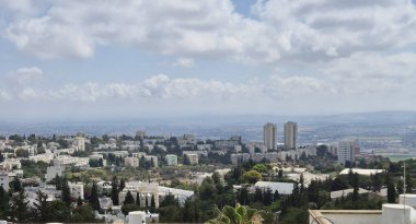 Konut binaları, tepeler ve dramatik bulutlarla dolu bir gökyüzünün altında uzanan uzak şehir manzarası..