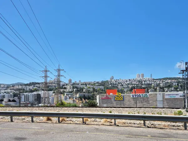 Hayfa, İsrail 24 Mayıs 2025: Elektrik kuleleri ve konut binaları Haifa 'daki yamaçta yer alıyor, altyapıyı canlı bir gökyüzü altında doğayla harmanlıyor.