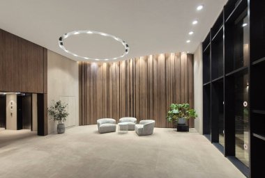 Modern bir lobide zarif kıvrımlı sandalyeler, ahşap panel duvarlar ve tavan ışıklarıyla aydınlatılmış dekoratif bitkiler bulunur..