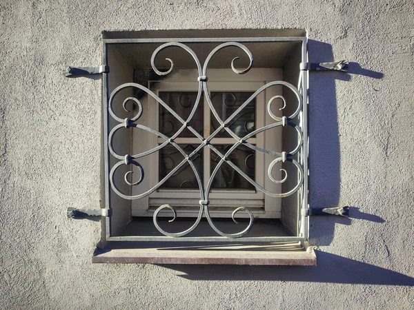 Beautiful old square window forged window security grate with long shadows on concrete building wall on sunny day