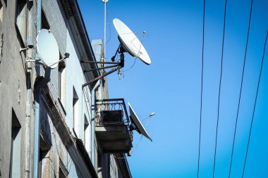 Beyaz uydu anteni antenleri çatıda ve eski binanın duvarında parlak mavi gökyüzü arka planında çizgiler ya da kablolar var.