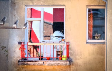 Çiçek saksıları olan eski bir apartman dairesi sağ taraftaki pencerede kırmızı beyaz bir tekstil sancağının yansıması ve soldaki aydınlatma.