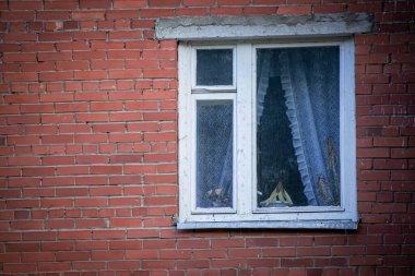 Kırmızı tuğladan duvarda plastik çerçeveli Avrupa tarzı kirli pencere pervazda ve dantel perdelerde ölü ev bitkileri var.