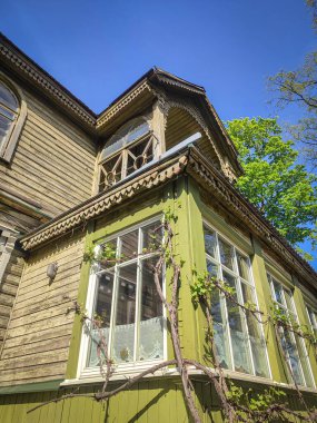 Mavi gökyüzü arka planında büyük pencereleri olan eski ahşap bir evin köşesi, güneşli bir günde alt manzarası