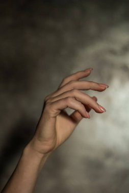 Gri arkaplanlı, seçici odaklı, basit bir manikürlü, güzel bir kadın elinin yakın çekimi. Uzun parmaklar ve narin bir bilek, plastik hareket.