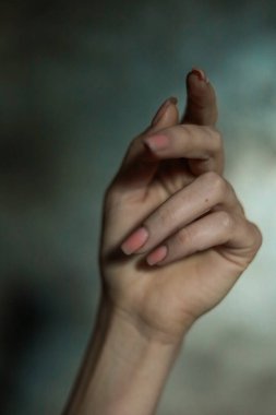 Gri arkaplanlı, seçici odaklı, basit bir manikürlü, güzel bir kadın elinin yakın çekimi. Uzun parmaklar ve narin bir bilek, plastik hareket.
