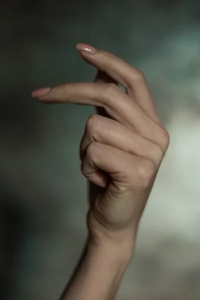 シンプルなネイルマニキュアで美しい女性の手のクローズアップ 灰色の背景に 選択的な焦点 長い指と壊れやすい手首 プラスチック製の動きを織ります — ストック写真