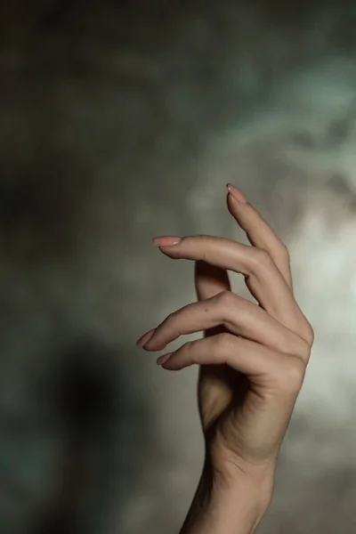 stock image Close-up of a beautiful female hand with a simple nail manicure, on a gray background, selective focus. Weave long fingers and a fragile wrist, plastic movement.