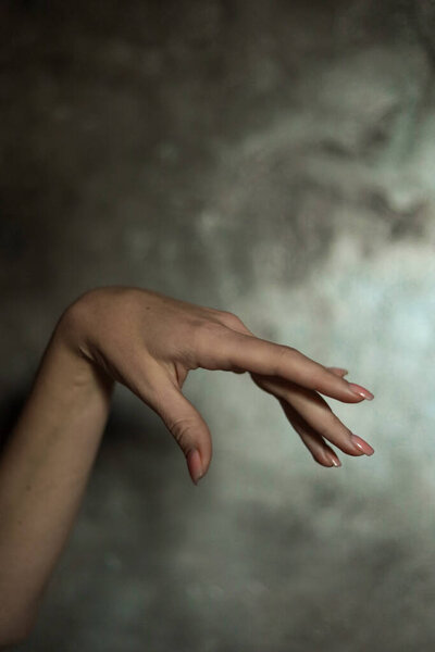 Close-up of a beautiful female hand with a simple nail manicure, on a gray background, selective focus. Weave long fingers and a fragile wrist, plastic movement.