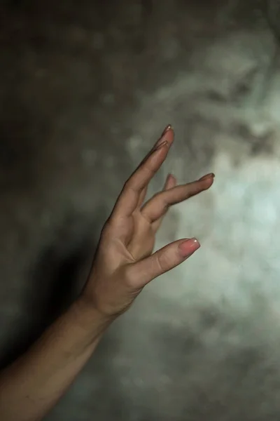 stock image Close-up of a beautiful female hand with a simple nail manicure, on a gray background, selective focus. Weave long fingers and a fragile wrist, plastic movement.