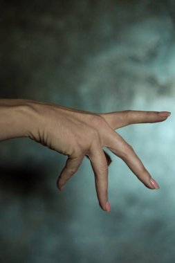 Gri arkaplanlı, seçici odaklı, basit bir manikürlü, güzel bir kadın elinin yakın çekimi. Uzun parmaklar ve narin bir bilek, plastik hareket.