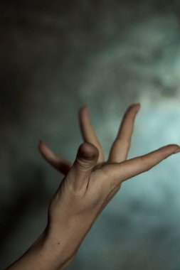 Gri arkaplanlı, seçici odaklı, basit bir manikürlü, güzel bir kadın elinin yakın çekimi. Uzun parmaklar ve narin bir bilek, plastik hareket.