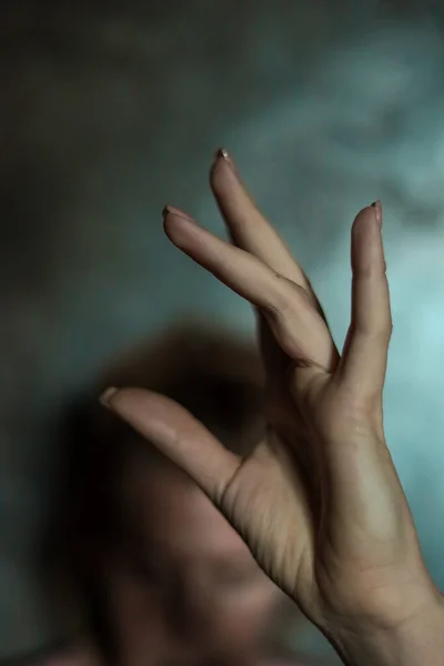 stock image Close-up of beautiful female hand with simple nail manicure on gray background, selective focus. Long fingers and a fragile wrist, plastic movement on the background of a face and a gray wall.