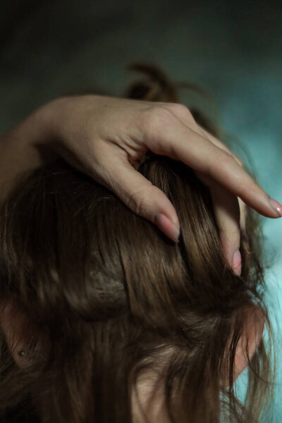 Крупный план красивой женской руки с простым маникюром ногтей на сером фоне, избирательный фокус. Длинные пальцы и хрупкое запястье, пластиковые движения на фоне темных длинных рыжих волос.