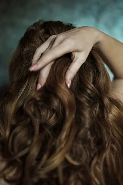 stock image Close-up of beautiful female hand with simple nail manicure on gray background, selective focus. Long fingers and fragile wrist, plastic movement against the background of dark long red hair.