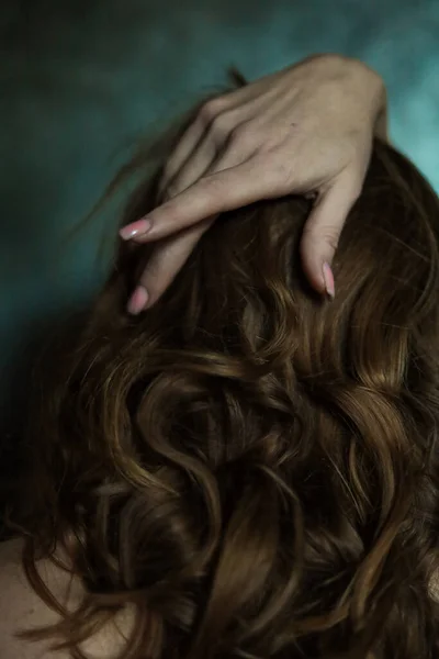 stock image Close-up of beautiful female hand with simple nail manicure on gray background, selective focus. Long fingers and fragile wrist, plastic movement against the background of dark long red hair.