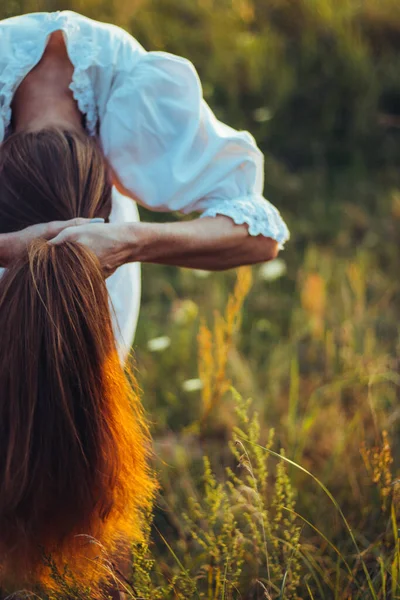 美しい長髪の女が太陽の光の下で髪を結ぶために曲げ 豪華な長い赤い健康的な髪 自然なケアと育成の概念 自然光 選択的焦点 — ストック写真