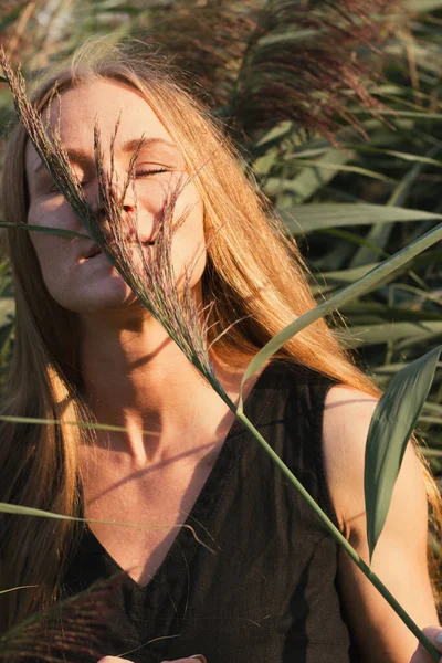 緑の葦に笑顔を舞う長い赤い髪をした黒のドレスの若い美しい少女の肖像画 自然の中で屋外でポーズ魅力的な女性 選択的フォーカス — ストック写真