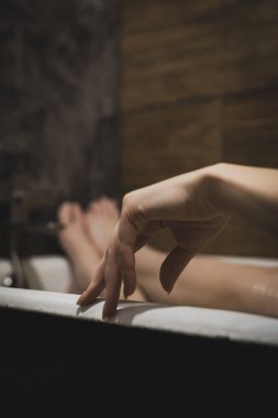 Ön planda doğal manikürlü, bacakları banyoda, uzanmış, rahatlamış, dinlenmiş güzel bir kadın avuç içi. Cilt bakımı için SPA prosedürleri, mutlu kadın. Güzel arkaplan, seçici odak, yakın plan.