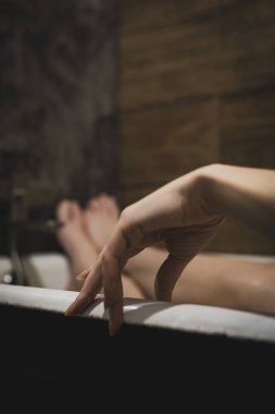 Ön planda doğal manikürlü, bacakları banyoda, uzanmış, rahatlamış, dinlenmiş güzel bir kadın avuç içi. Cilt bakımı için SPA prosedürleri, mutlu kadın. Güzel arkaplan, seçici odak, yakın plan.