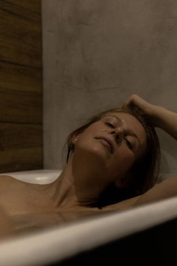 Küvette uzanıp güzellik ayininin tadını çıkaran mutlu bir kadın. Güzel bir kadın banyoda, sıcak suda dinleniyor. Temizlik, ev güzellik tedavileri, güzel bir geçmiş, seçici odaklanma..
