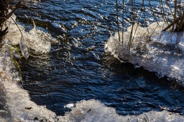 Suyun üzerindeki buzlu buzlar. Buz, buz sarkıtları ve kalıpların oluştuğu Soğuk Nehir. Güneşli bir gün, parlıyor, parlıyor. Güzel doğal arkaplan, doğal doku.
