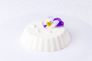 Panna cotta beyaz arka planda yenilebilir mor çiçekle dekore edilmiştir.