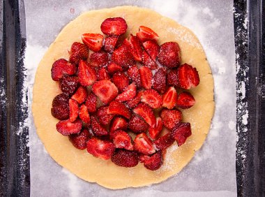 Çilekli turta galet pastası hazırlığı. Çilekli çiğ hamur, parşömen kağıdının üstünde, fırın tepsisinin üzerinde. Üst görünüm