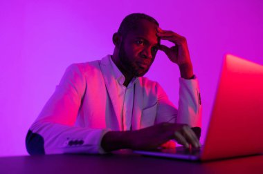 A black programmer works using a laptop computer. the man works at night. office with neon lighting
