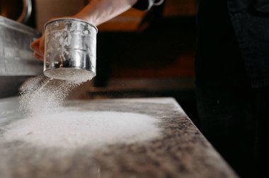Close-up of a boy in the kitchen pours and sows flour through a metal sieve into. Home baking concept. The process of making pie, pizza